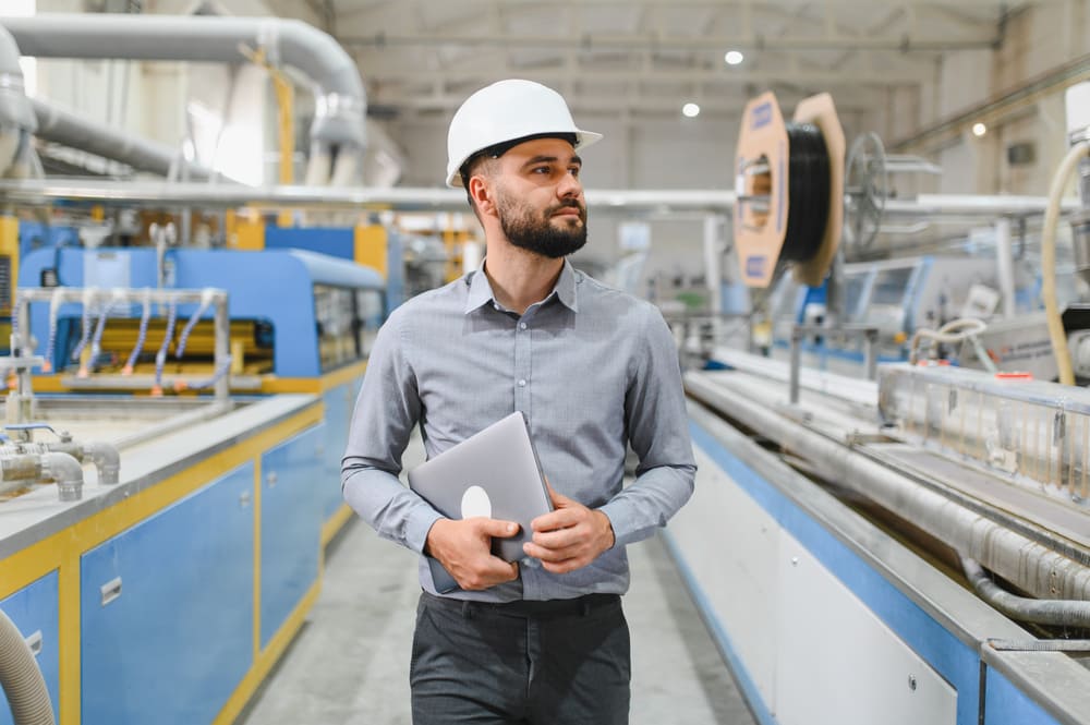 Profissional utilizando notebook em chão de fábrica industrial, representando a aplicação do lean manufacturing, gestão eficiente de processos e acompanhamento operacional em tempo real.