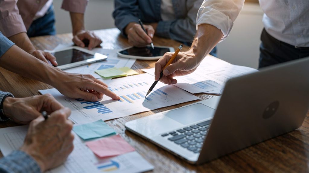 Equipe corporativa analisando relatórios financeiros e indicadores de desempenho em reunião estratégica sobre expansão internacional e gestão integrada de operações.