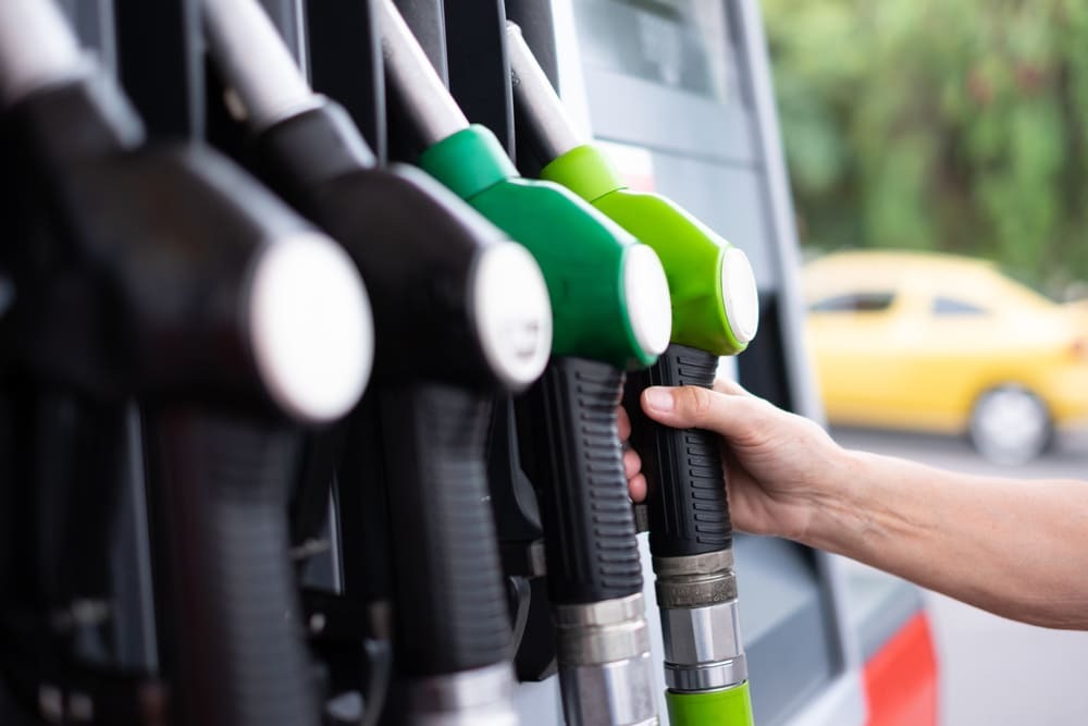 Pessoa segurando bico de combustível em posto de gasolina, representando custos de viagem e a importância de saber como saber quantos pedágios tem na rota ao planejar deslocamentos.