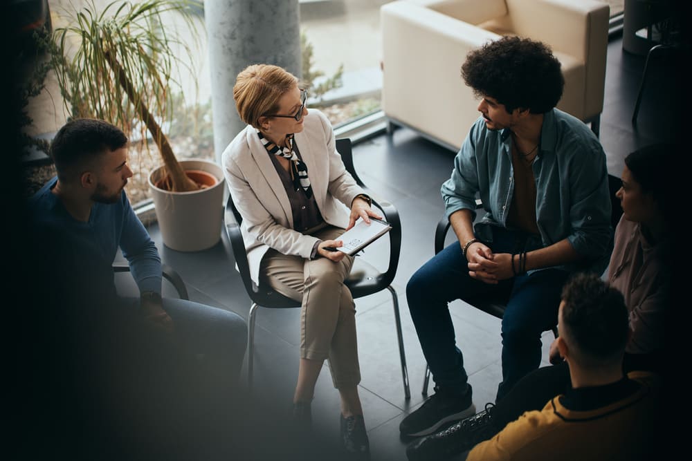 Grupo de colaboradores em conversa mediada por especialista, representando ações de prevenção, acolhimento e suporte relacionados à síndrome do burnout nas empresas.