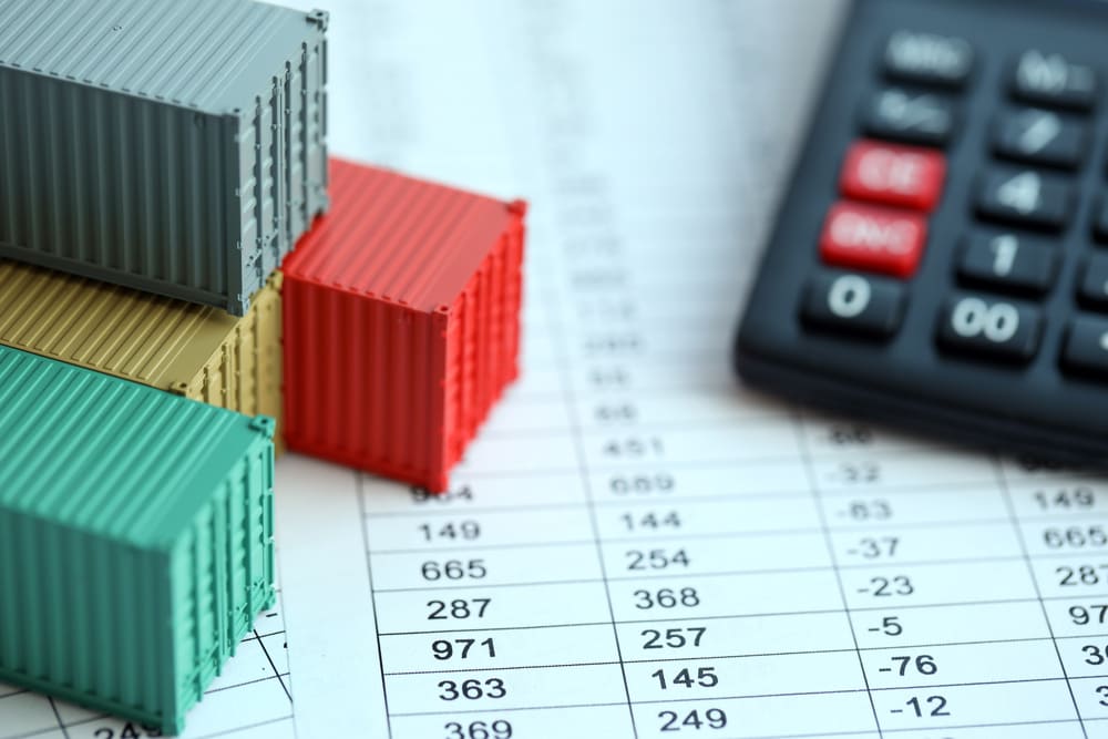 Containers coloridos em miniatura posicionados sobre papel com números e calculadora, utilizados para gerenciar importação e exportação de produtos.