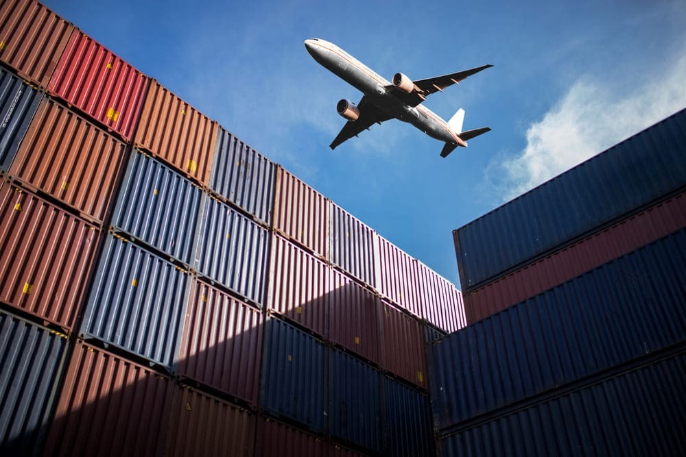 Avião sobrevoando containers, fazendo o transporte internacional de cargas para empresas de logística.