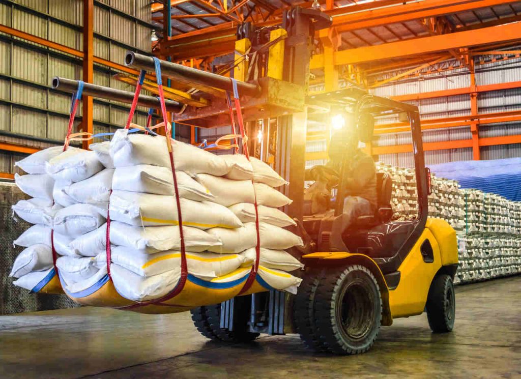Empilhadeira transportando sacas de commodities agrícolas em galpão logístico industrial do agronegócio brasileiro