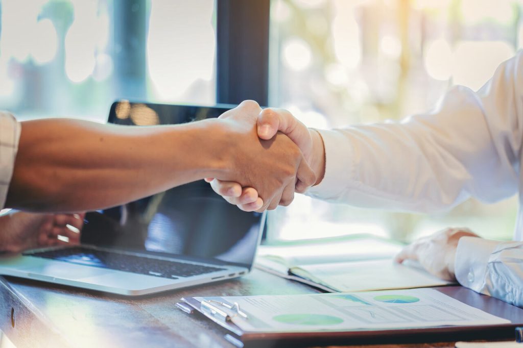 Aperto de mãos entre profissionais após acordo contratual, representando formalização e negociação de aditivo de contrato.