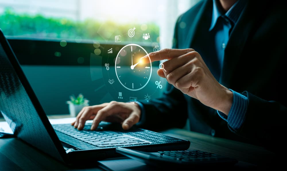 Pessoa em ambiente de escritório utilizando notebook com interface de relógio virtual, ilustrando o controle de ponto online.