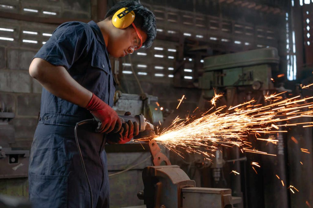 Trabalhador industrial operando uma ferramenta de corte em ambiente fabril, representando a produção local e o fortalecimento da manufatura com o reshoring.