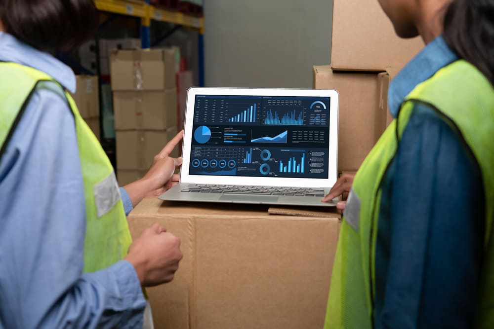 Profissionais em um armazém analisando dashboards em um notebook, exemplificando o uso de big data na logística para tomada de decisão e controle operacional.