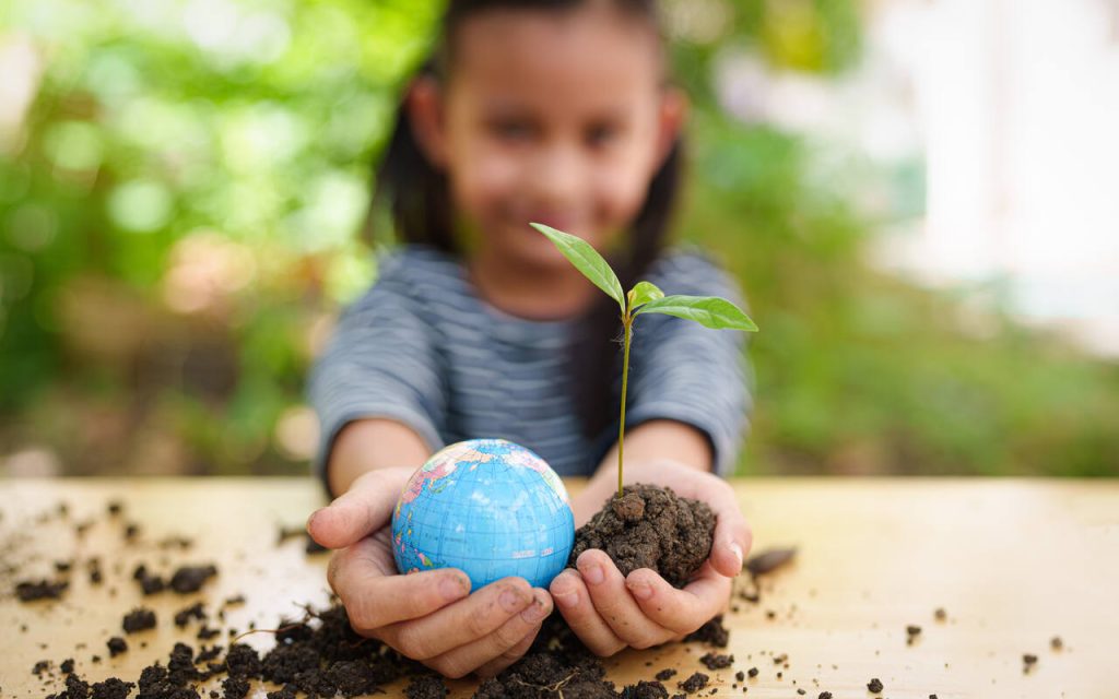 Criança segurando uma planta e um globo terrestre, representando a relação entre educação infantil e sustentabilidade ambiental