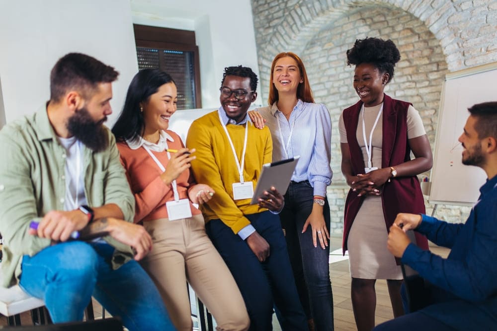 Equipe diversa rindo e interagindo em ambiente corporativo, enquanto líder aplica ferramentas de avaliação comportamental para entender o perfil dos colaboradores.