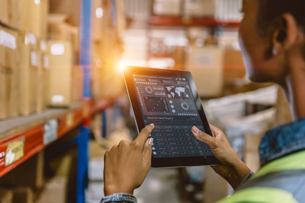 Profissional utilizando um tablet com sistema WMS para monitorar e gerenciar operações logísticas dentro de um armazém.