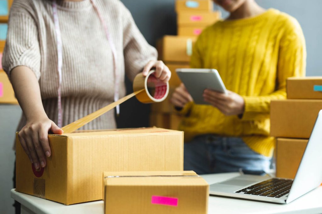 Pessoas embalando pedidos para envio, representando a logística e a preparação de produtos vendidos em marketplaces.