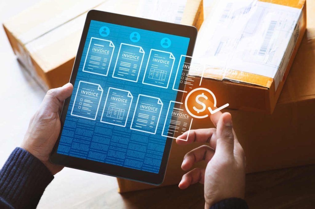 Tablet exibindo documentos digitais e informações financeiras, com caixas de encomendas ao fundo, representando a digitalização de processos e o uso de dados na logística.