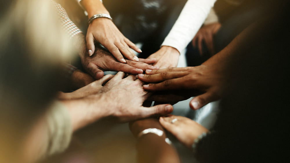 Grupo de pessoas com as mãos unidas em sinal de cooperação, representando exemplos de rituais que fortalecem o senso de pertencimento e a união entre equipes.