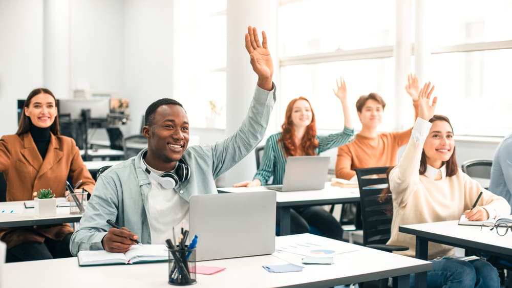 Estudantes em sala de aula levantando a mão durante apresentação de metodologias ativas de aprendizagem