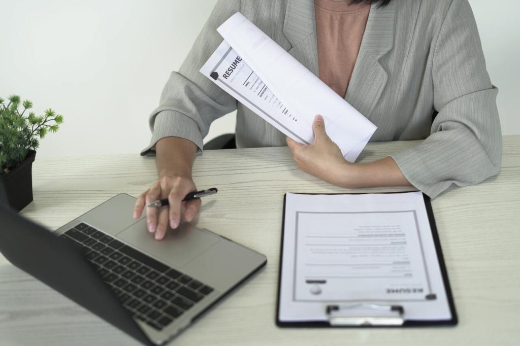 Mesa de trabalho com currículos, notebook e documentos, simbolizando a organização e análise de currículos durante a triagem no recrutamento.