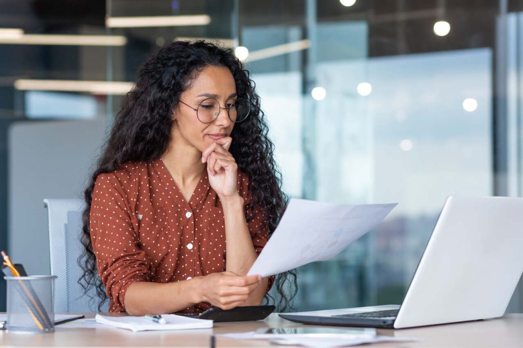 Profissional de RH analisando um currículo impresso no escritório, representando a etapa de triagem de currículos no processo de recrutamento e seleção.