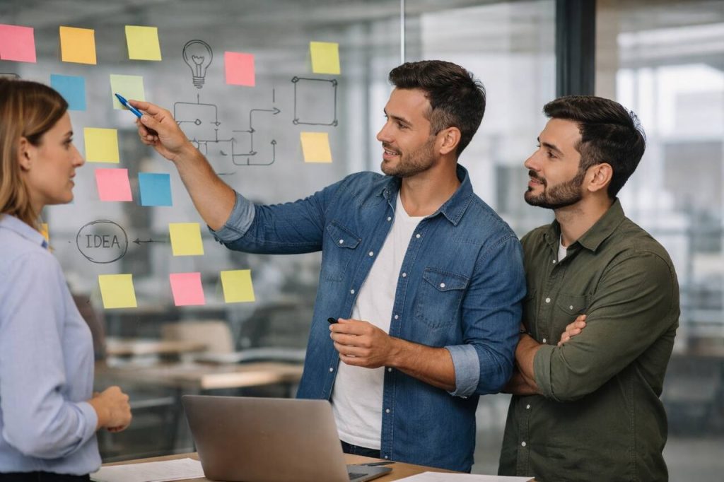 Equipe discutindo desenvolvimento de produto com post-its em quadro de vidro durante planejamento de MVP