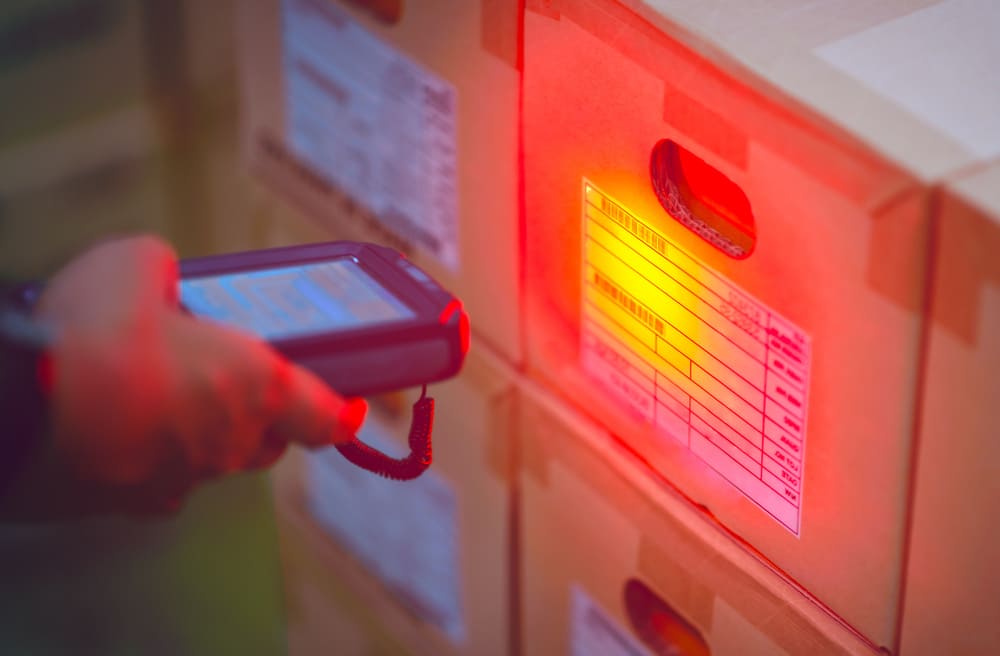 Pessoa segurando leitor portátil realizando a identificação de uma etiqueta RFID em caixas de armazenamento.