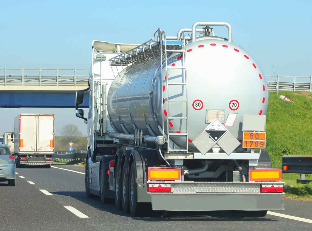 Caminhão-tanque transportando combustível em rodovia com sinalização de carga perigosa