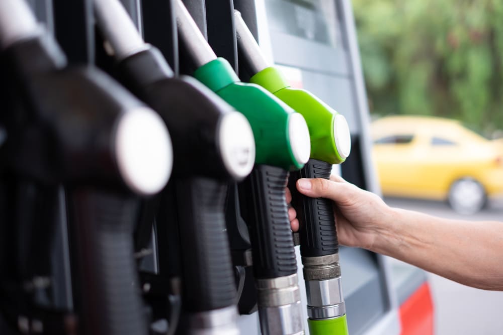 Pessoa segurando bico de combustível em posto de gasolina, representando custos de viagem e a importância de saber como saber quantos pedágios tem na rota ao planejar deslocamentos.