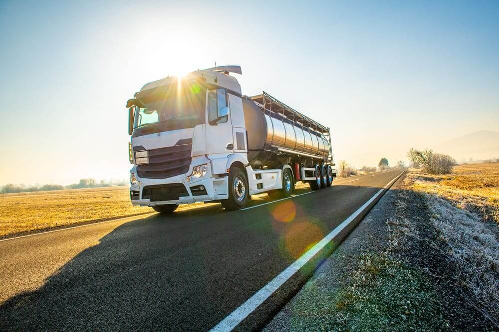 Caminhão-tanque branco trafegando em rodovia durante o amanhecer, um dos tipos de caminhões utilizados no transporte de cargas líquidas.