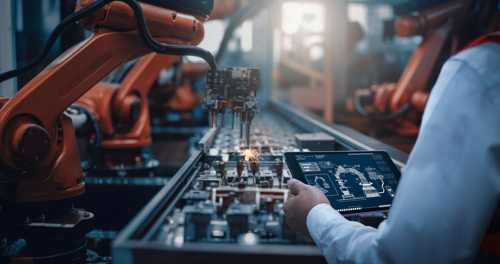 Linha de produção automatizada com robôs industriais e profissional monitorando dados em tablet, ilustrando tendências e aplicações da physical AI na indústria.