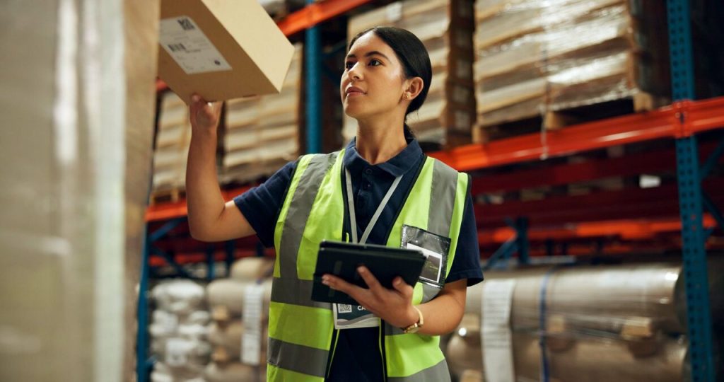 Profissional de logística conferindo mercadoria em centro de distribuição com apoio de sistema ERP para gestão de estoque
