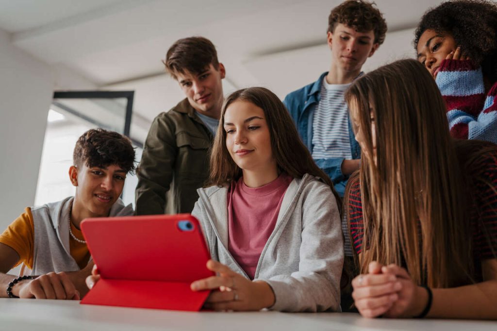 Grupo de estudantes interagindo em torno de tablet em sala de aula, exemplo de aprendizagem ativa e atividades interativas na escola
