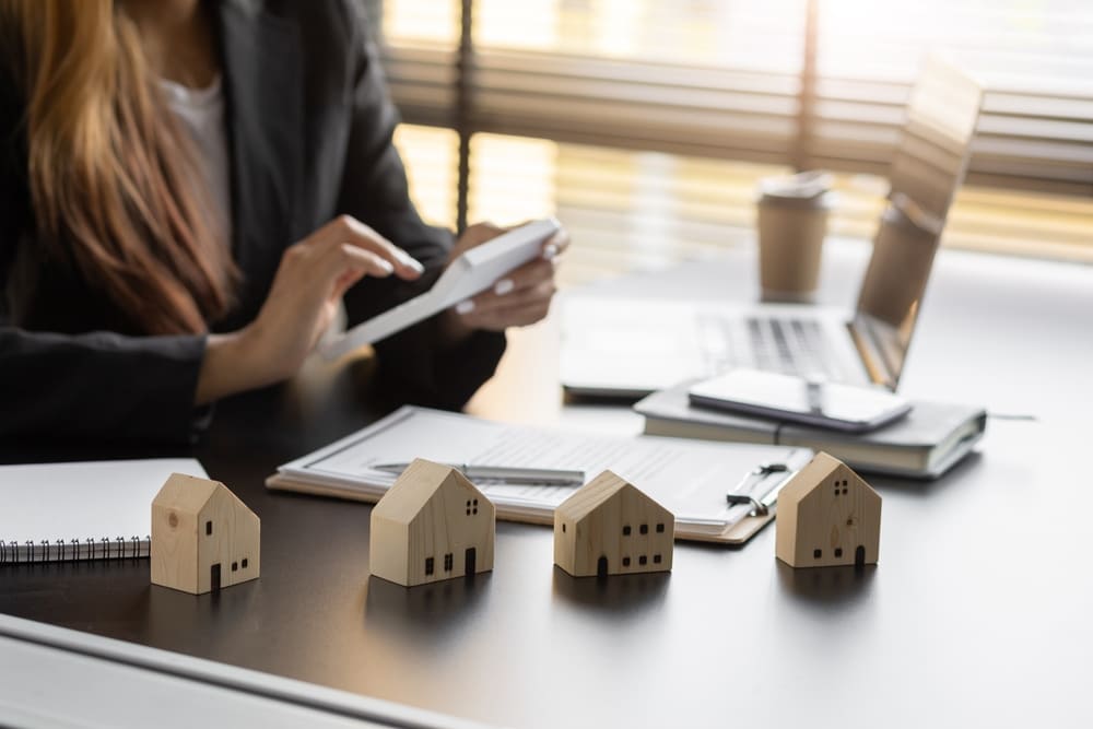 Profissional analisando dados em tablet com miniaturas de casas na mesa, avaliando os principais desafios das imobiliárias no Brasil.