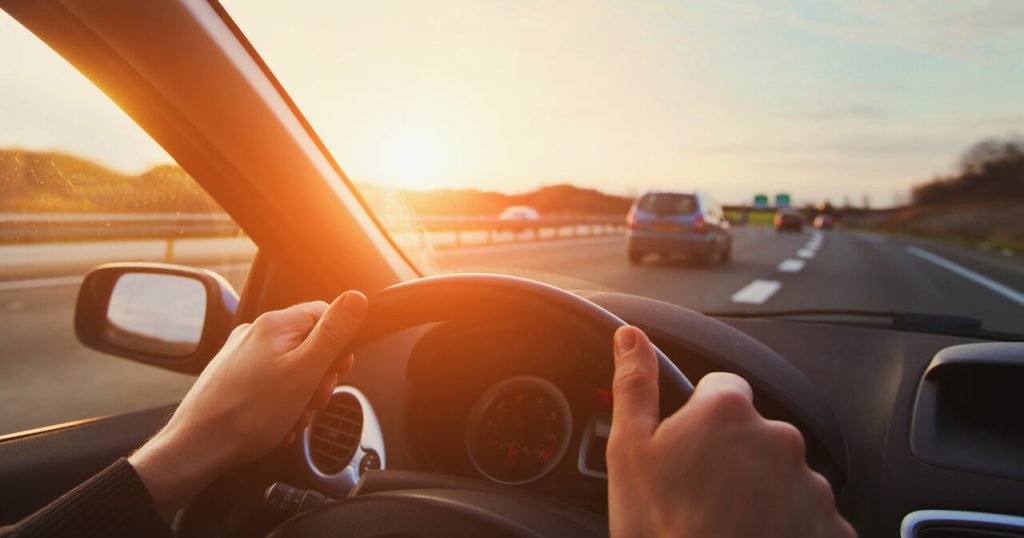 Motorista dirigindo carro em rodovia ao pôr do sol, representando segurança no trânsito e boas práticas de condução