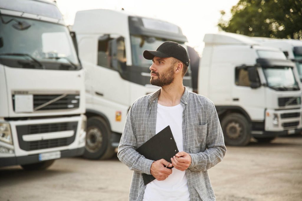 Motorista de caminhão com prancheta em frente à frota analisando requisitos para autorização especial de trânsito (AET)