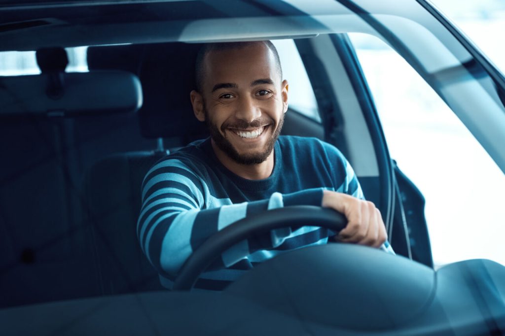 Motorista dirigindo carro e sorrindo ao volante em ambiente urbano