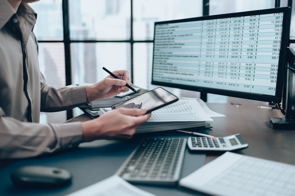 Pessoa analisando dados financeiros no computador e documentos fiscais, cenário que representa na prática o que é ISSQN e como calcular o imposto sobre serviços