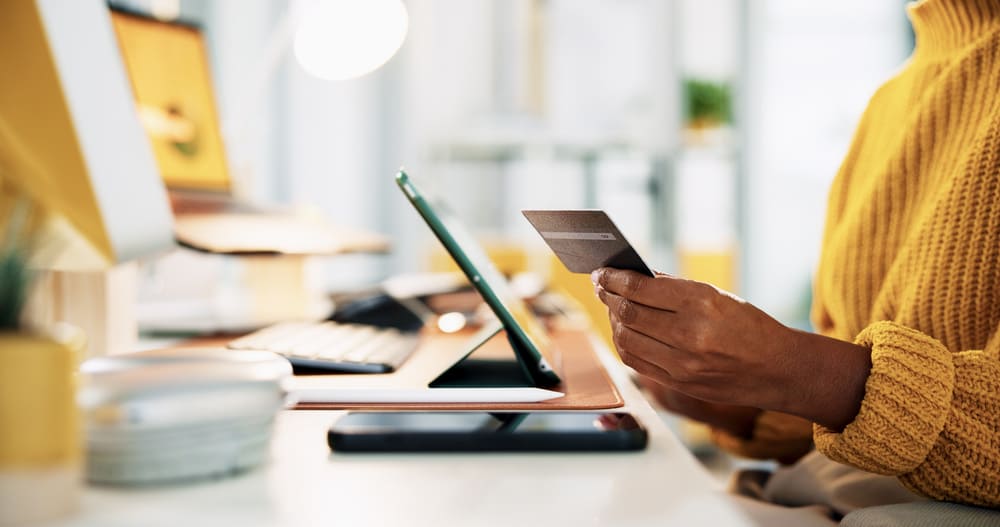 Mulher segurando cartão e utilizando tablet para gerenciar conta PJ e realizar operações financeiras empresariais online.