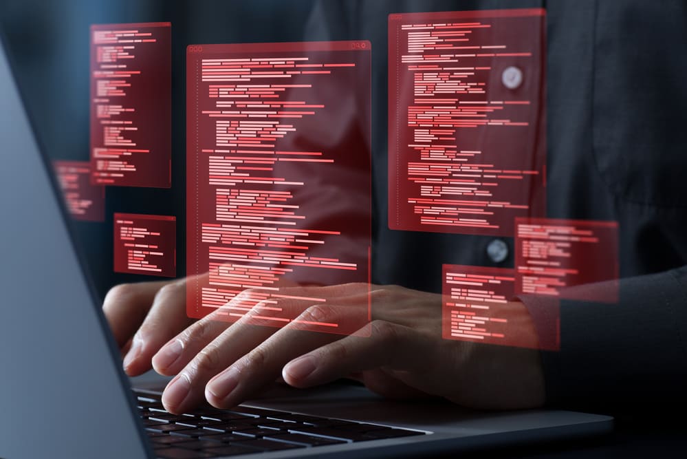 Tela com códigos em vermelho sendo manipulados em notebook, ilustrando os impactos e riscos de um ataque cibernético em sistemas corporativos.
