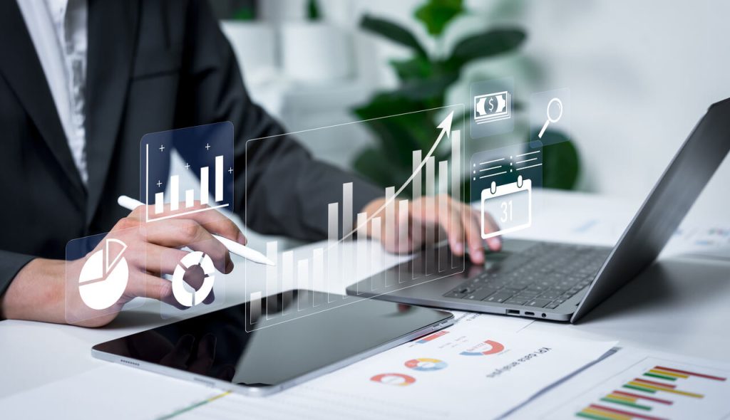 Profissional analisando dashboards e gráficos financeiros em notebook e tablet, representando o uso de ferramentas de BI e análise de dados nas empresas.