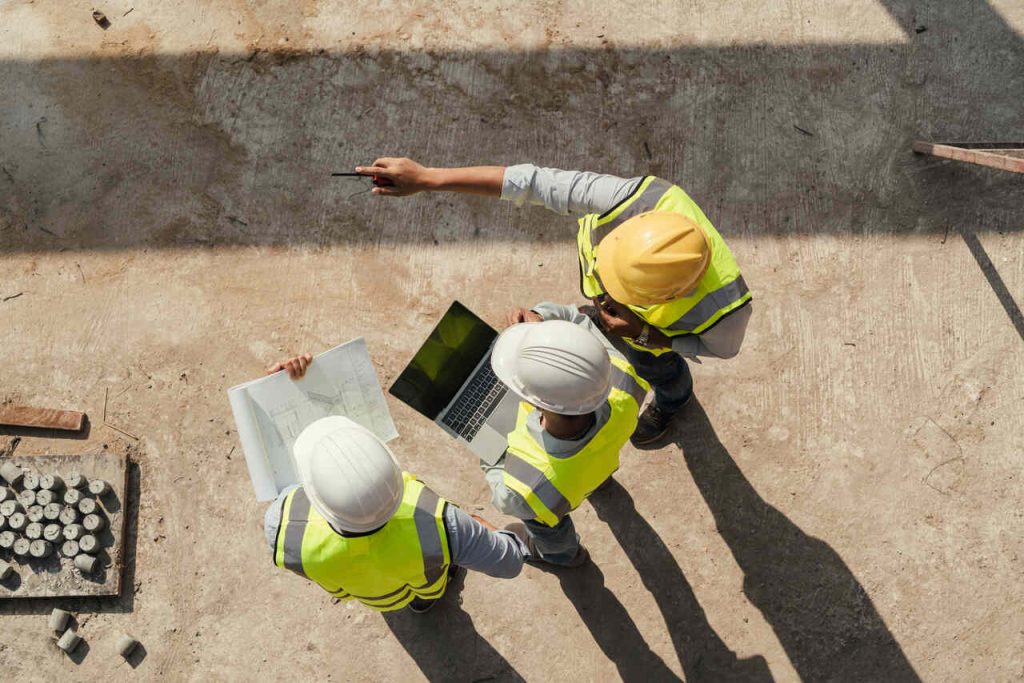 Profissionais de segurança do trabalho analisam riscos em canteiro de obras utilizando plantas e computador durante a elaboração do PGR.