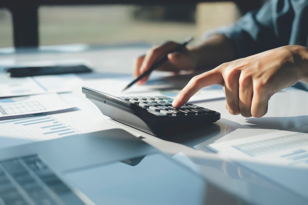 Pessoa utilizando uma calculadora sobre documentos financeiros para realizar o cálculo do imposto, representando o planejamento tributário necessário para a emissão do ITR em propriedades rurais.